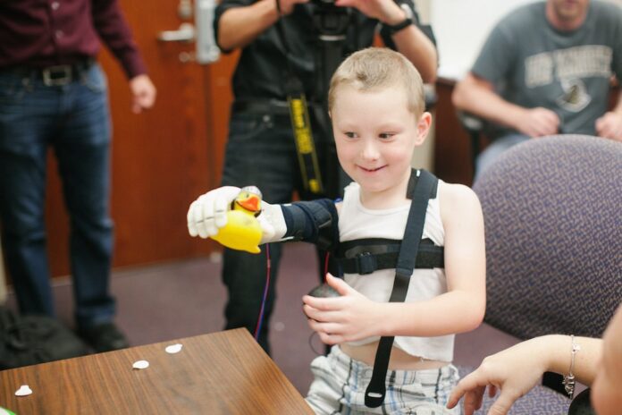 5d08f52d95e8375b1c81d00a_Limbitless a boy using the robotic arm to pick up a toy duck-min
