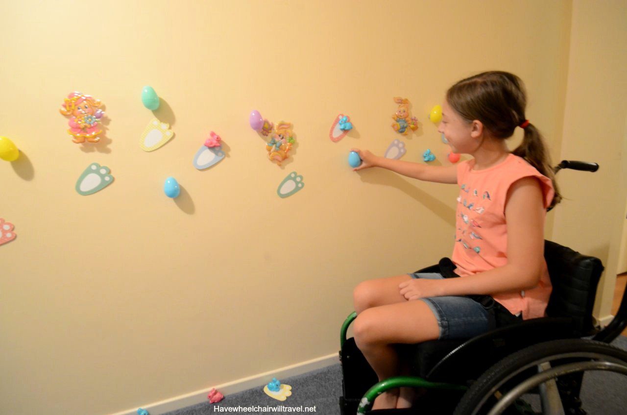 Photo of girl, in a wheelchair, participating in an adaptive Easter egg hunt (on wall); courtesy of https://havewheelchairwilltravel.net/