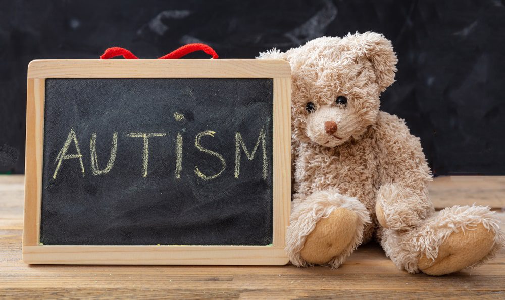 "autism" written on chalkboard, with teddy bear beside it