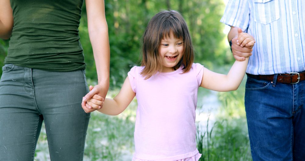girl with down syndrome walking hand-in-hand between two adults