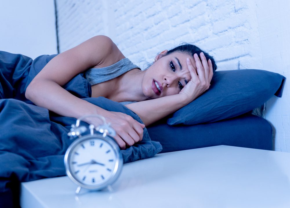 woman lying in bed with clock in front of her