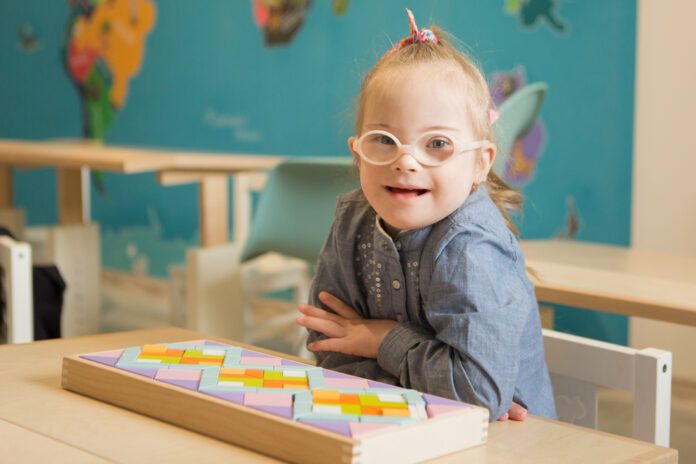 Girl with Down syndrome, wearing pink glasses, seated in classroom