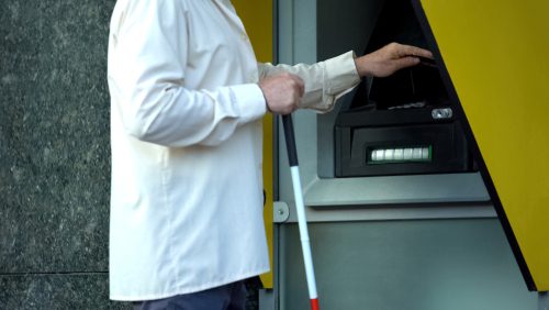 blind man, holding stick in one hand, and using ATM with other