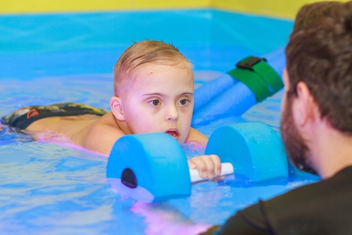 Boy, with Down syndrome, practicing swim safety with an instructor in a pool.
