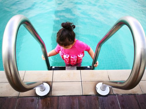 Girl, who has autism, wears a swim vest while entering a pool.